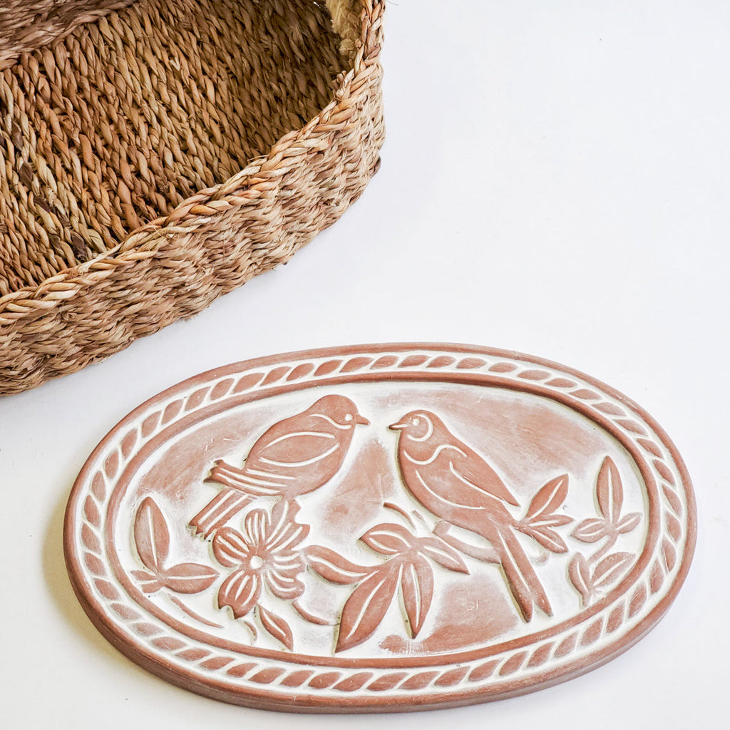 Ceramic plate with bird design next to a woven basket on a white background