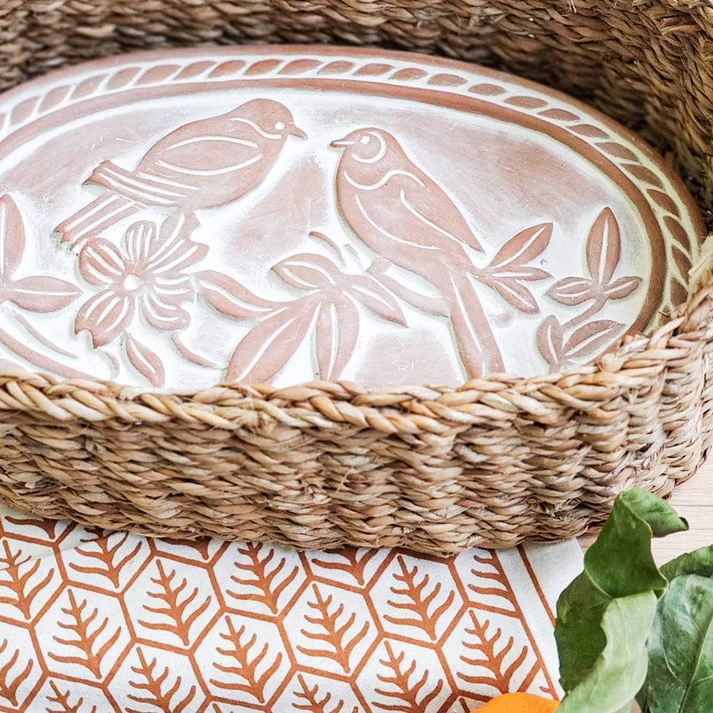 Decorative plate with bird design on a woven basket and patterned tablecloth with pumpkin and bread.