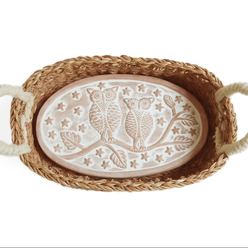 Decorative plate with owl design in a woven bread warmer basket on a white background