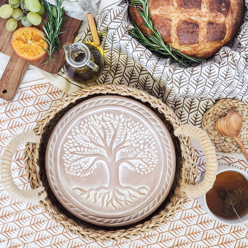 Baked bread with herbs, a cutting board with fruit, and a decorative plate with a tree design on a patterned tablecloth.